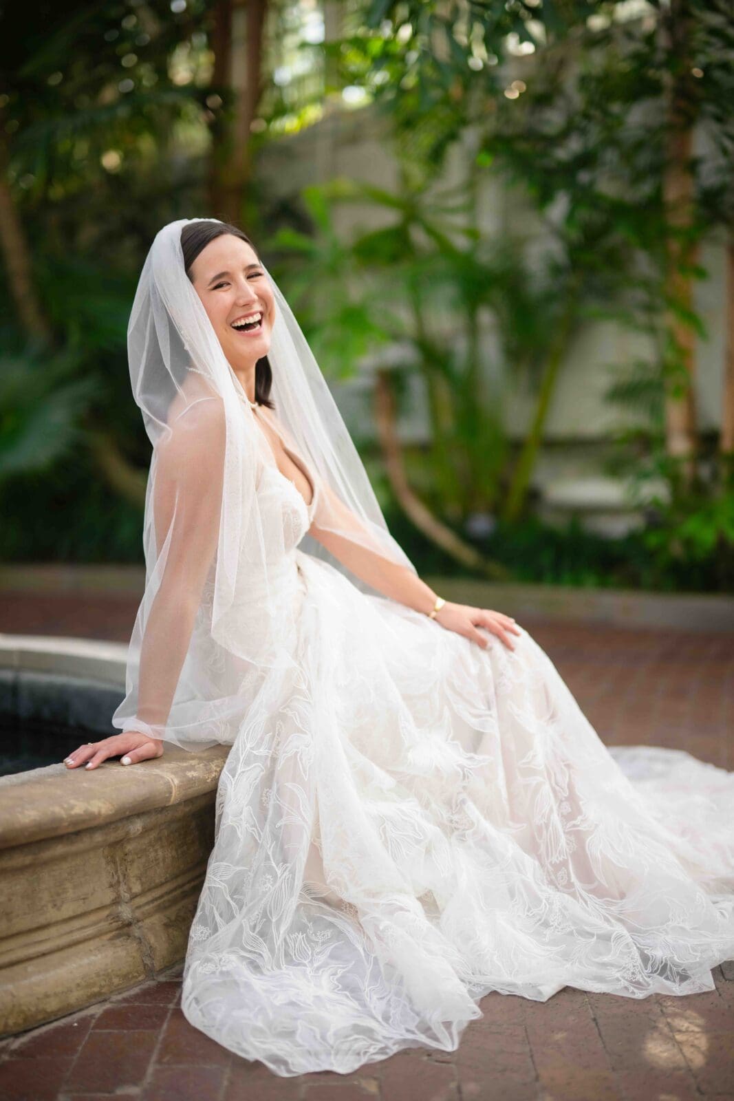 bride laughs joyfully sitting on fountain in palm house at Franklin Park Conservatory
