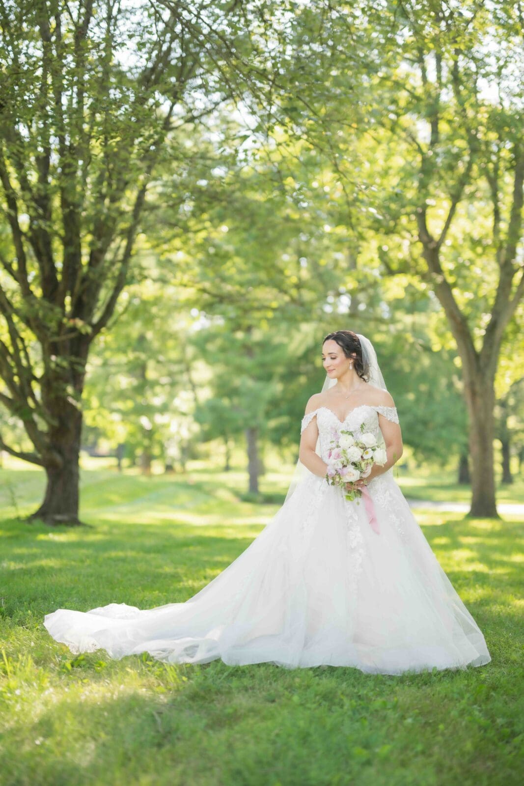 Bride wearing wedding dress with long train posing outside in greenery at Darby House