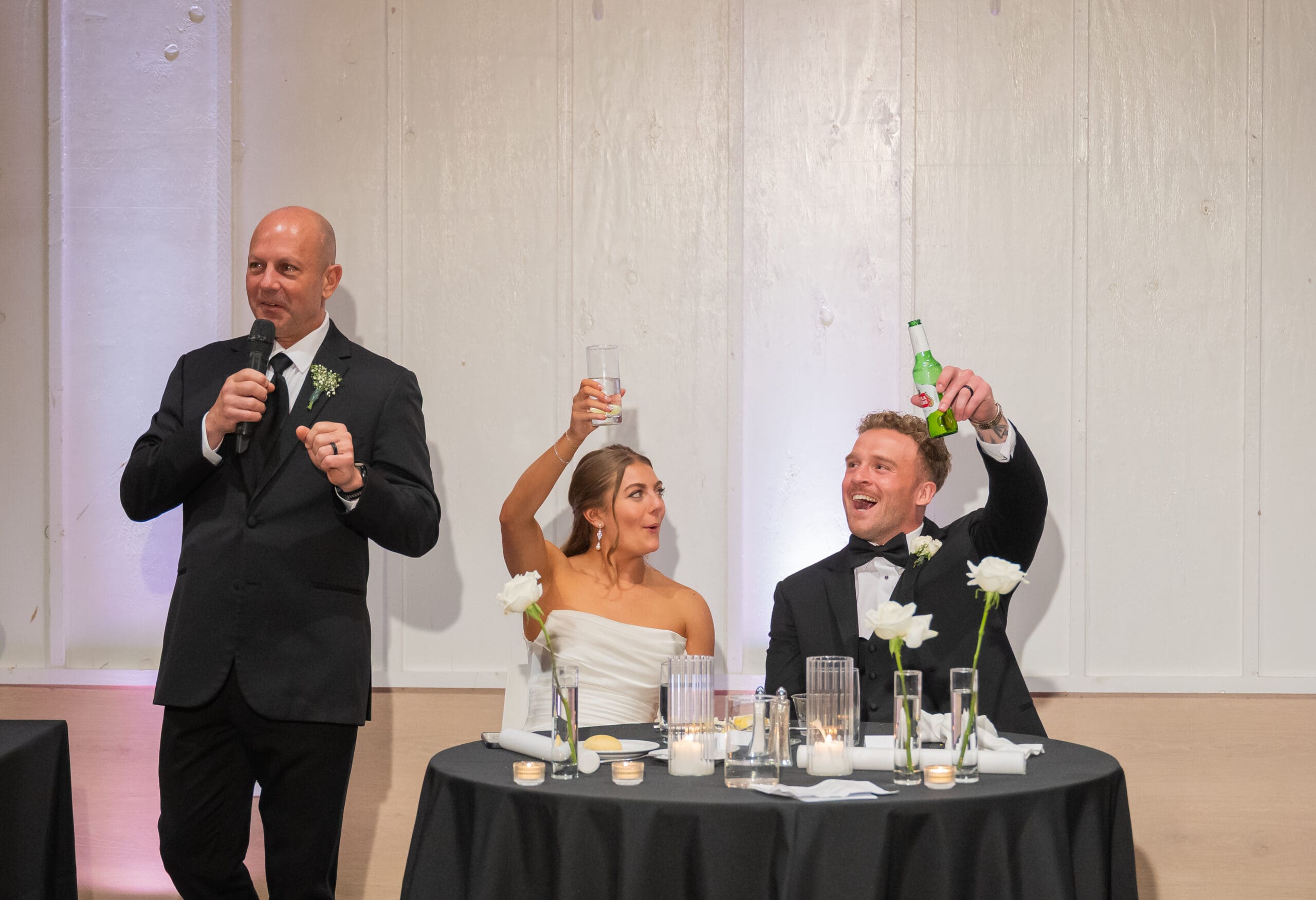 Couple raising glasses and smiling as dad is giving wedding day toast at Retreat 21