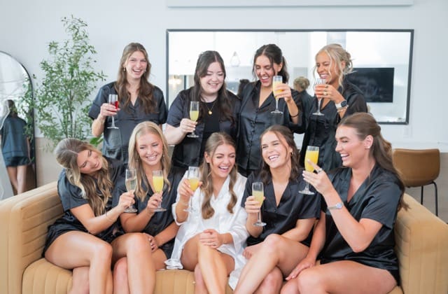 Bridesmaids and bride with drinks and sitting on couch in matching pajamas at Retreat 21